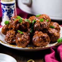 3 ingredient cranberry meatballs on a white serving plate with sliced green onions garnishing the meatballs.