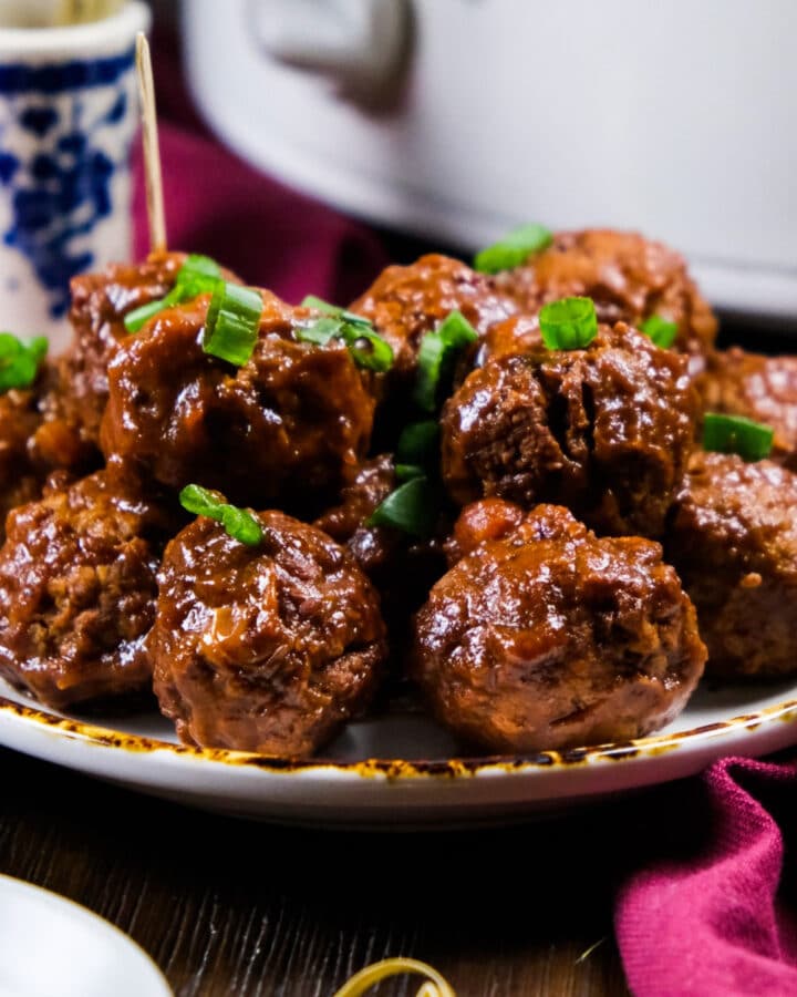3 ingredient cranberry meatballs on a white serving plate with sliced green onions garnishing the meatballs.
