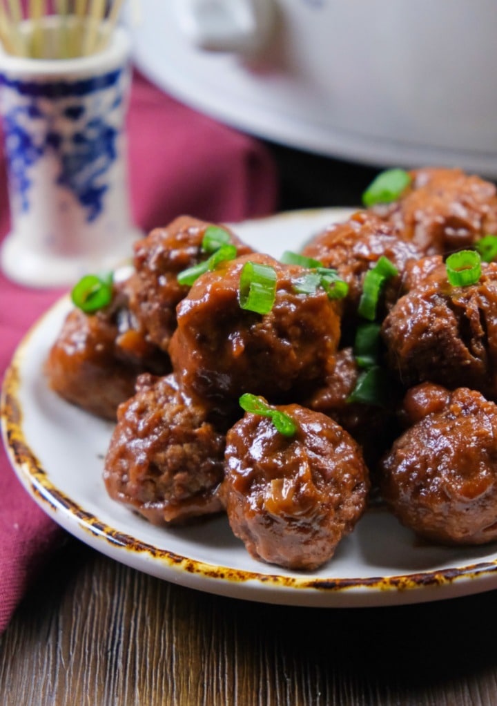 A small white serving plate filled with 3 ingredient cranberry meatballs topped with diced green onion. 