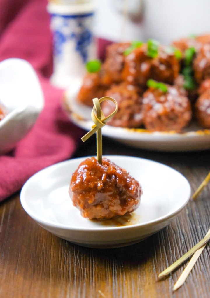 Cooked meatball with a skewer on a small white appetizer plate ready to eat. 