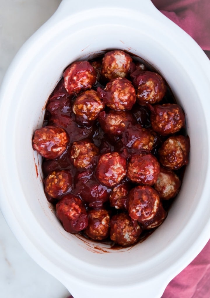 Meatballs covered in cranberry bbq sauce ready to cook in a crock pot. 