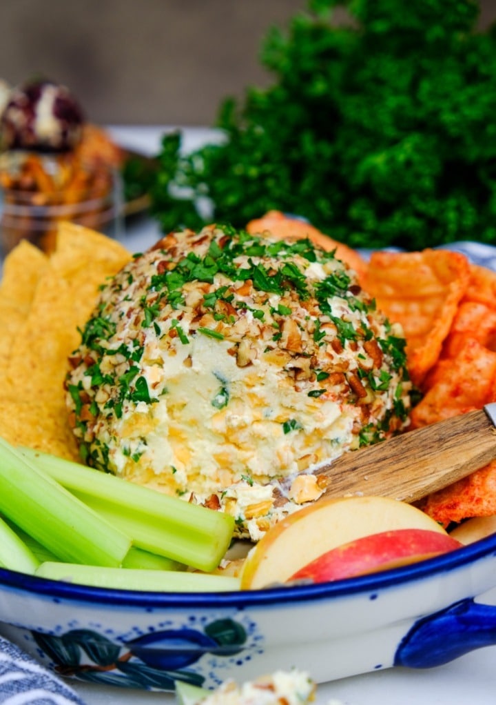 Cheese ball in a serving dish with celery and sliced apples.