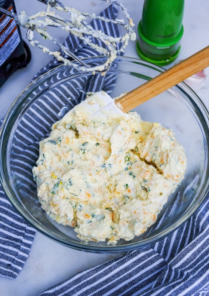 All cream cheese ball ingredients mixed with a hand mixer in a clear bowl. 