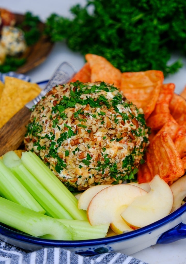 Low carb cheese ball on a platter with celery, apple slices and pork rinds. 