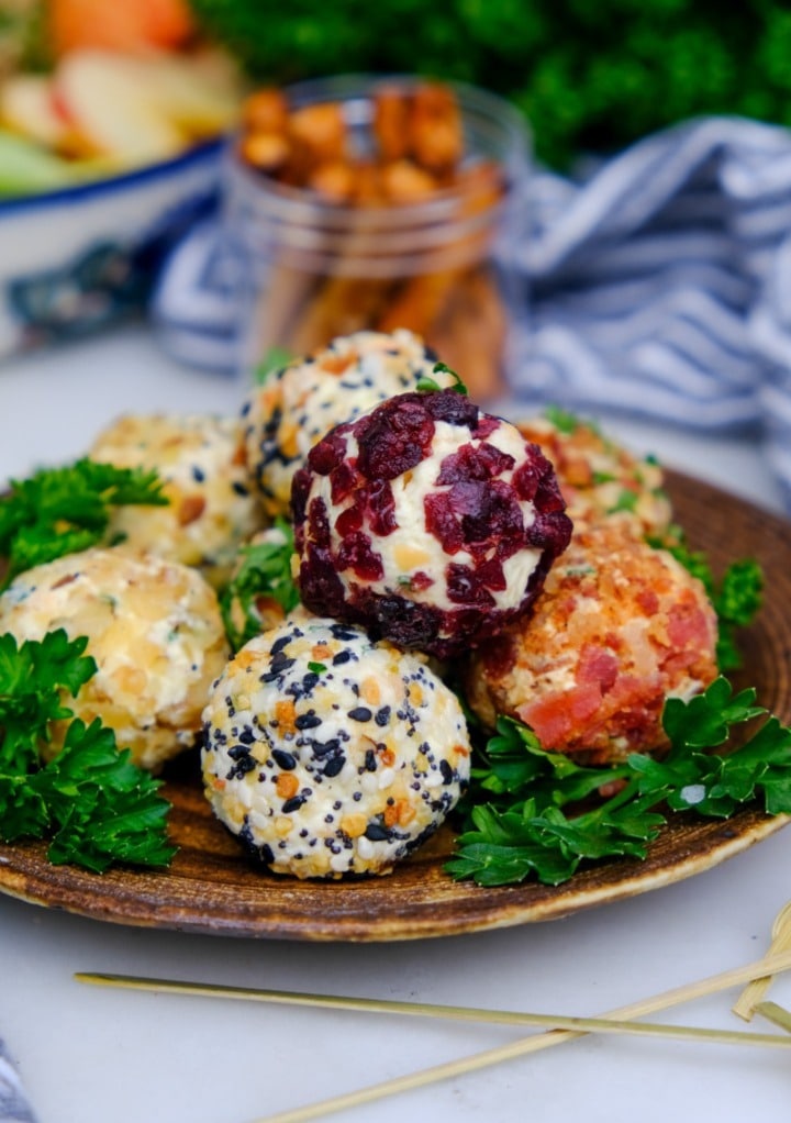 mini cheese ball bites rolled in different nuts and spices on a small brown serving plate.