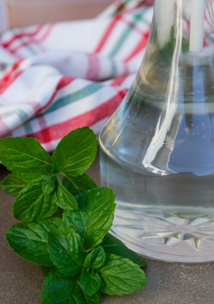 Fresh mint leaves next to a glass jar of peppermint syrup. 