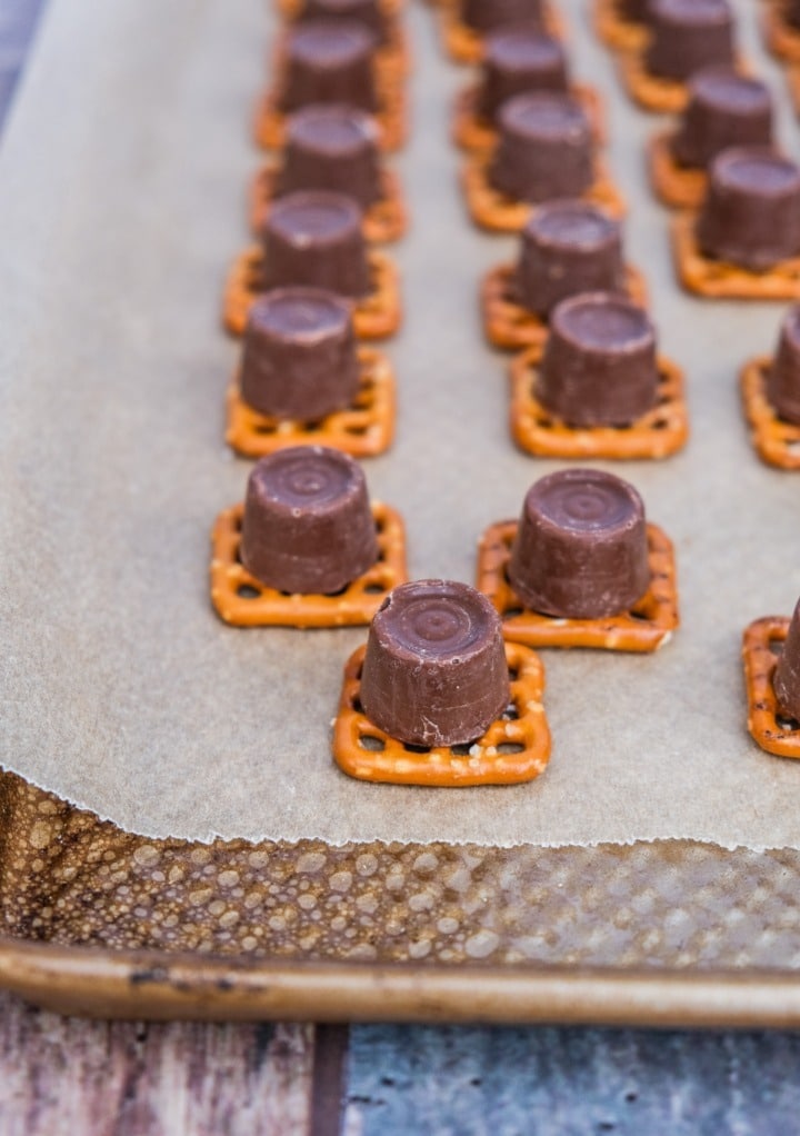 Rolo candy on a mini square pretzel placed on a baking sheet lined with parchment paper.