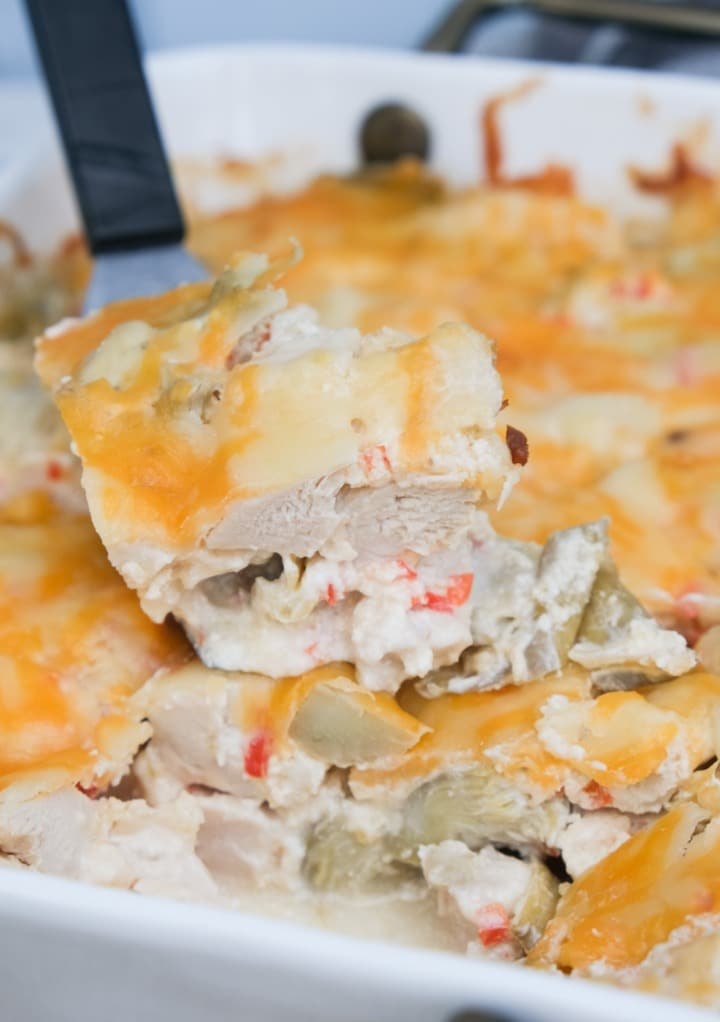 A slice of keto chicken artichoke casserole in a white baking dish ready to serve. 