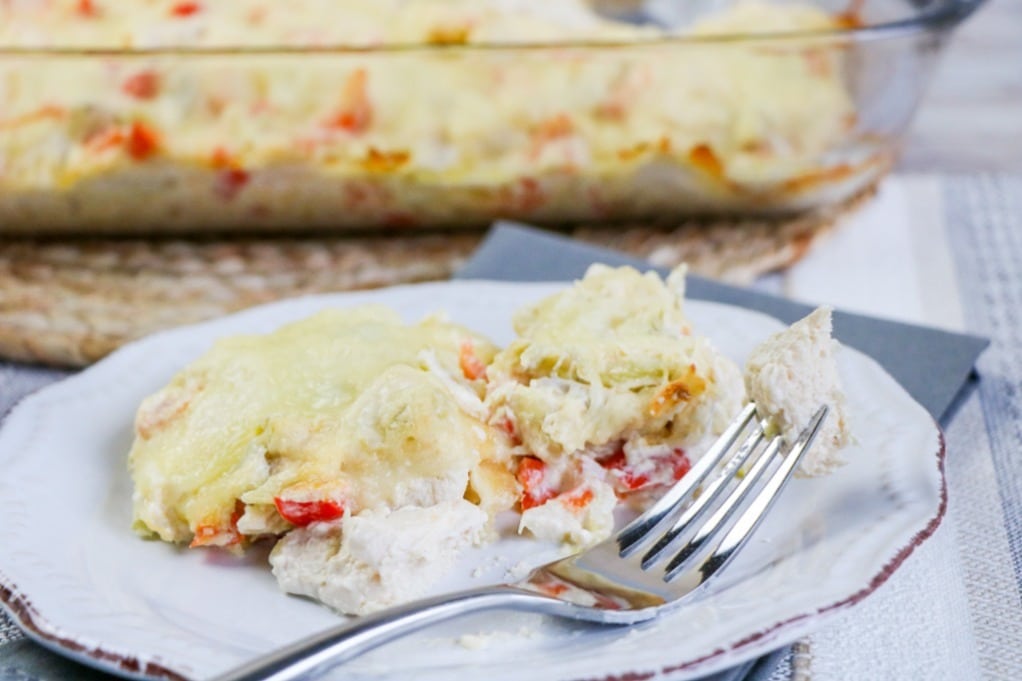 Slice of casserole on a white plate with a fork on the side ready to eat. 