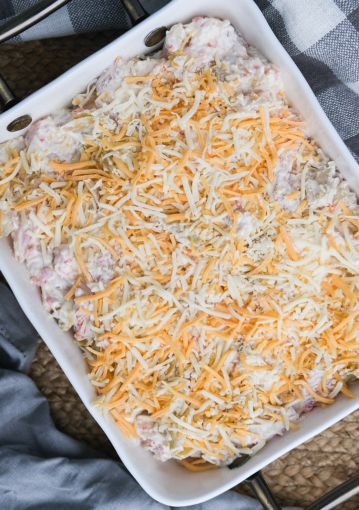 Chicken casserole in a baking dish with shredded cheese before baking. 