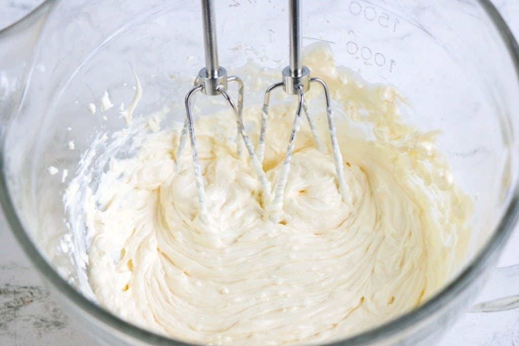 Cream cheese and mayonnaise blended with a hand mixer in a clear mixing bowl. 