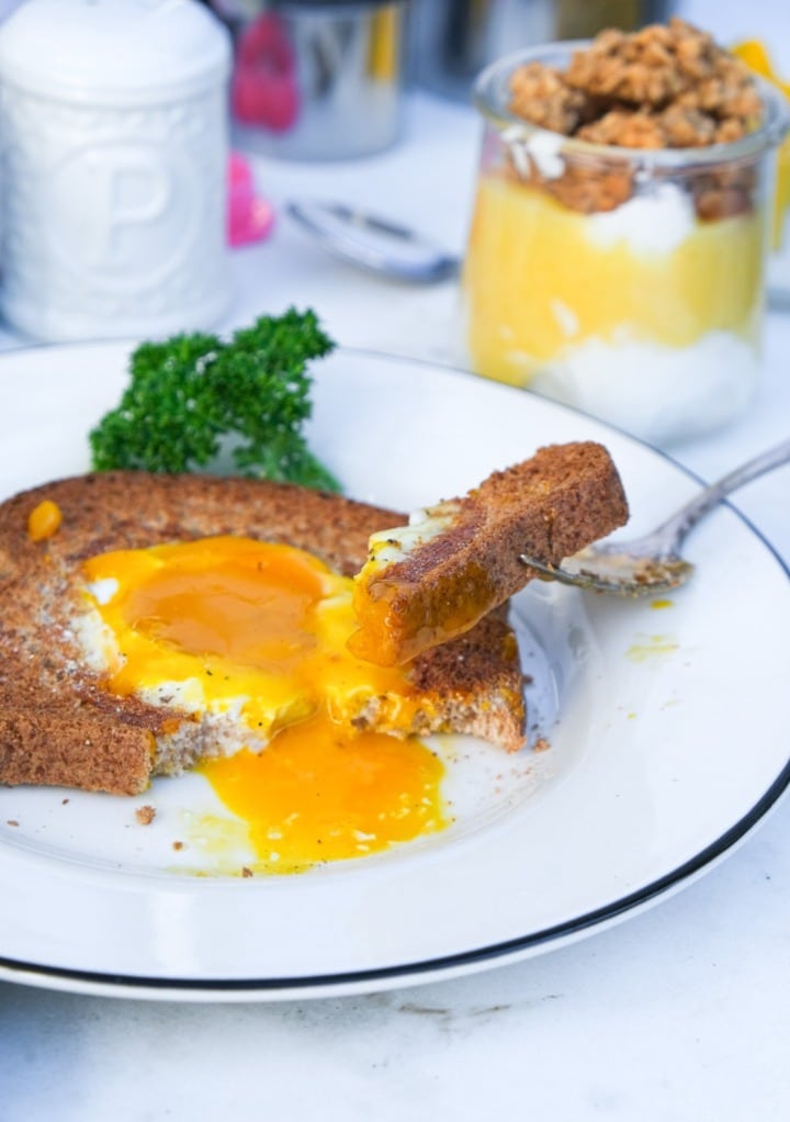A close view of a cooked egg in a hole with a fork grabbing a bite. 
