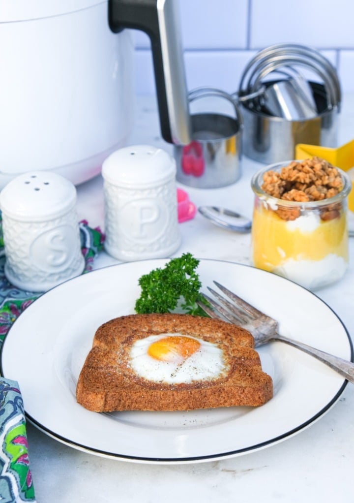 Air fryer egg in a hole dish on a white plate with salt and pepper shakers on the side. 