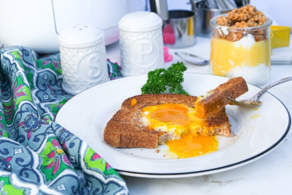 Toast with an egg cooked in the center with a piece of the toast in the yolk ready to eat. 