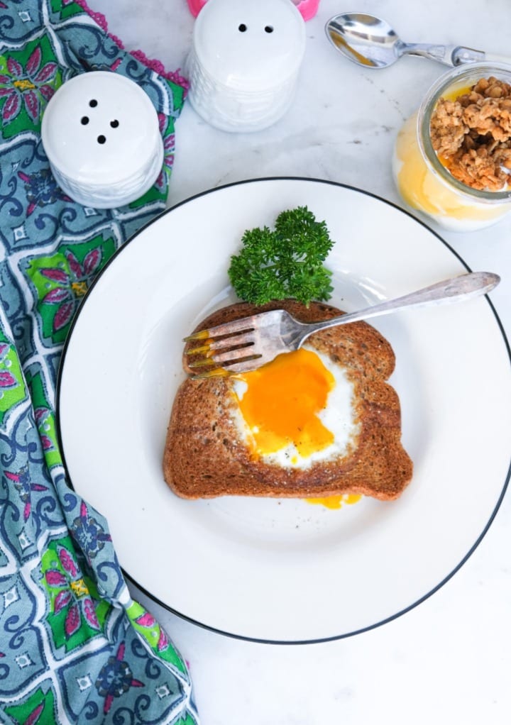 Top view of egg in a hole on a white plate with a black rim. 