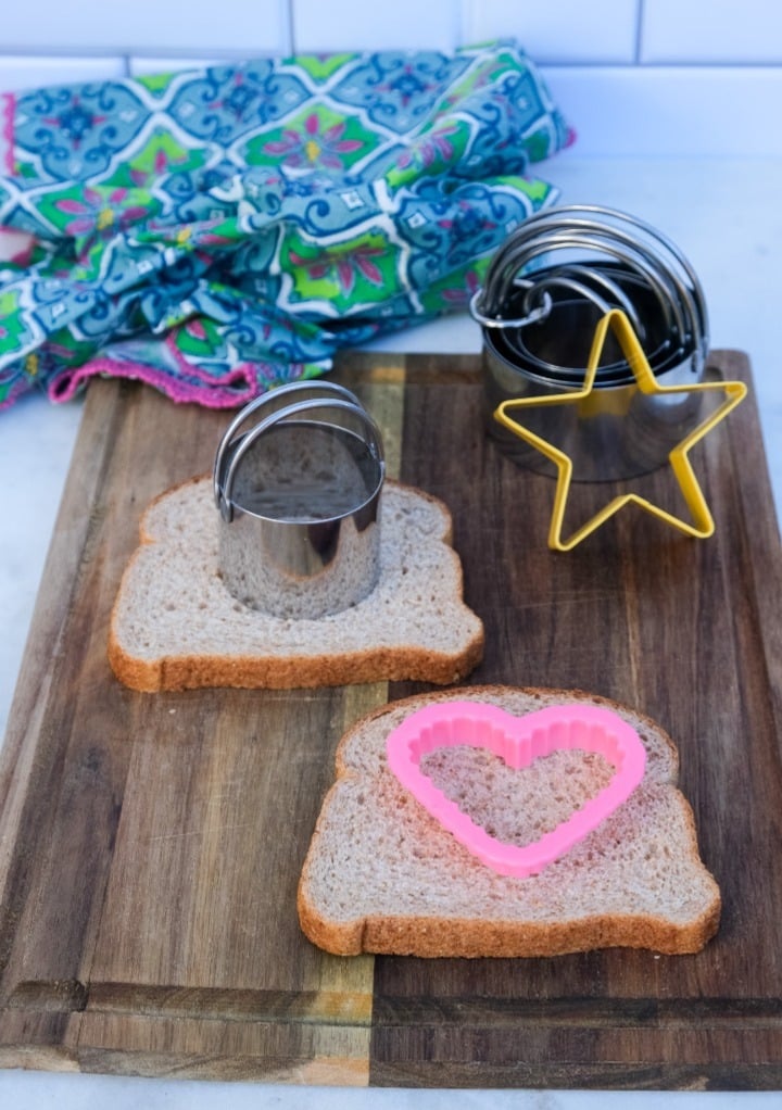 Sandwich bread on a cutting board with cookie cutters placed in the center of the bread to cut.