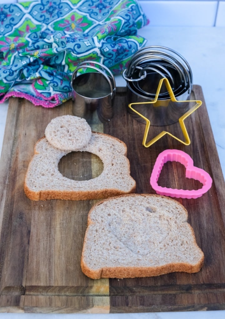 Sliced bread on a cutting board with the center cut out and the center indented to fit an egg to cook.