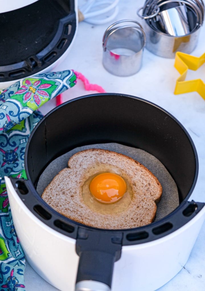 A slice of toast with an egg in the center placed in the insert of an air fryer. 