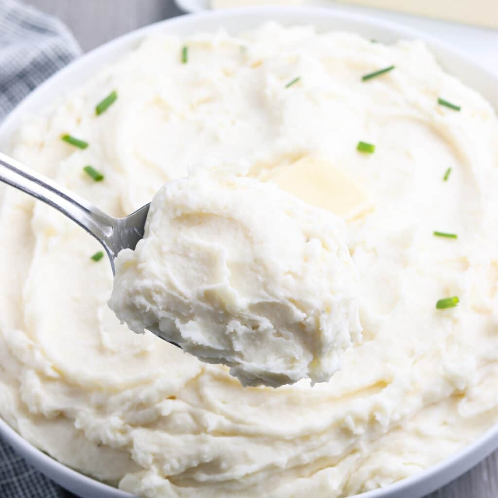 A spoonful of mashed potatoes in a white serving bowl.