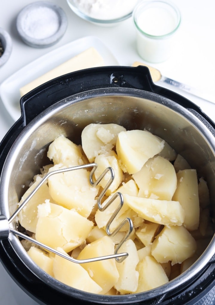 Cooked diced potatoes with a potato masher. 