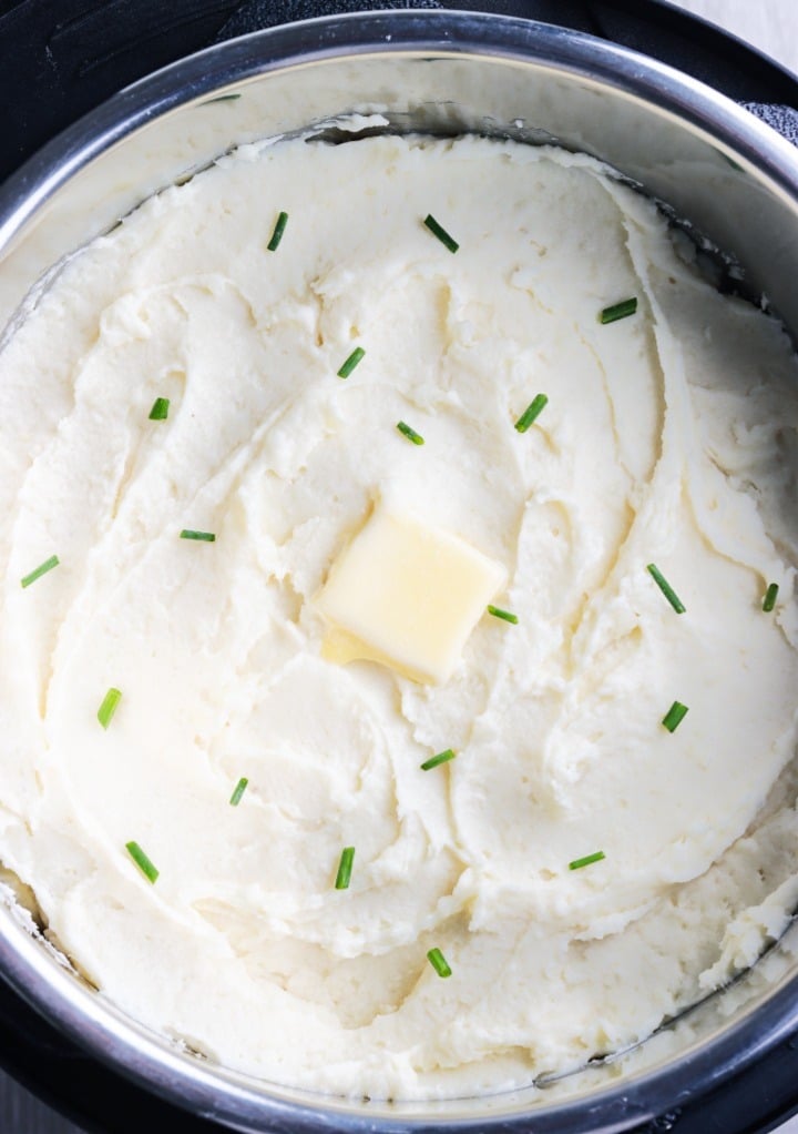 Creamy mashed potatoes in the insert of an Instant Pot with a pat of butter and diced chives. 