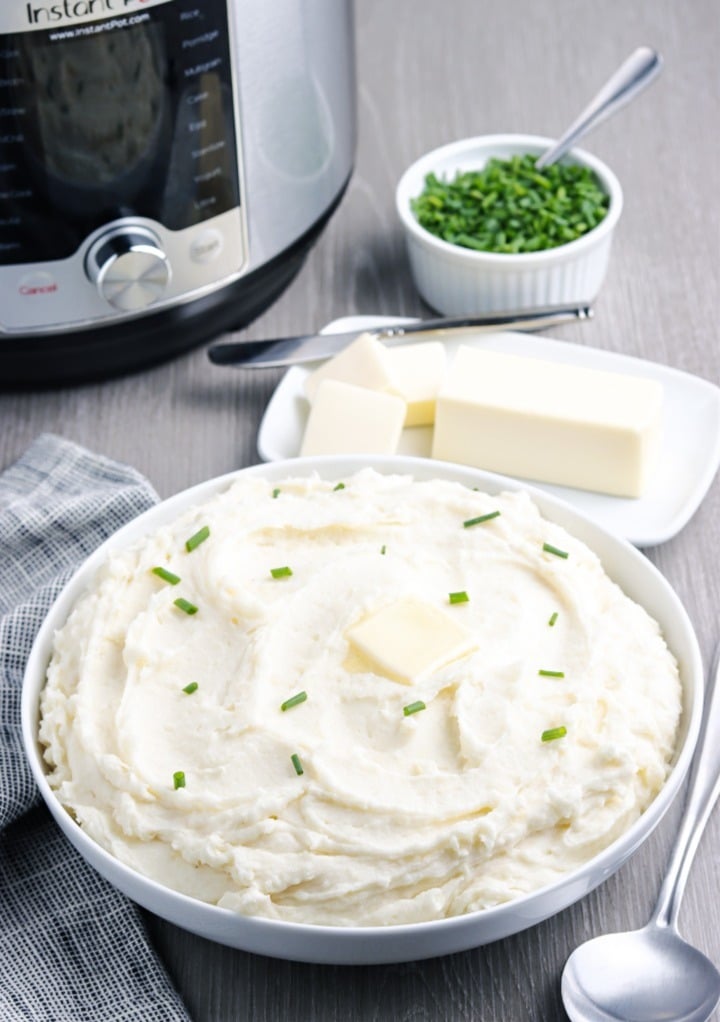 Mashed potatoes in a white serving bowl with an instant pot in the background. 