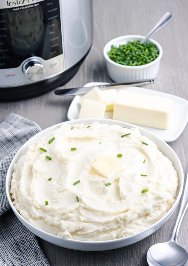 Mashed potatoes in a white serving bowl with an instant pot in the background.