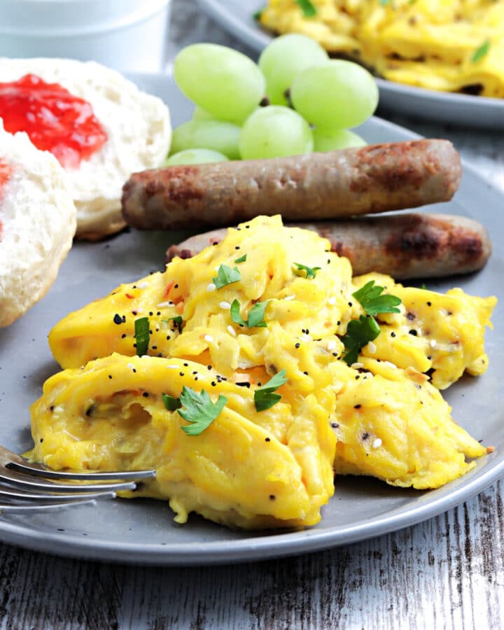Cooked scrambled eggs on a light blue plate with sausage and a sliced English muffin.