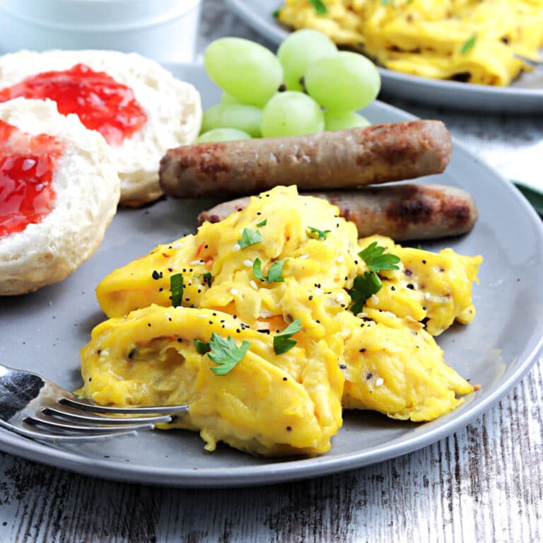 Cooked scrambled eggs on a light blue plate with sausage and a sliced English muffin.