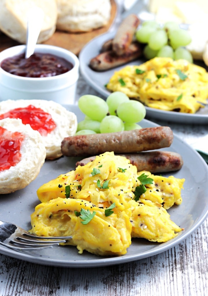 Breakfast plate with eggs, sausage and sliced muffin with jam. 