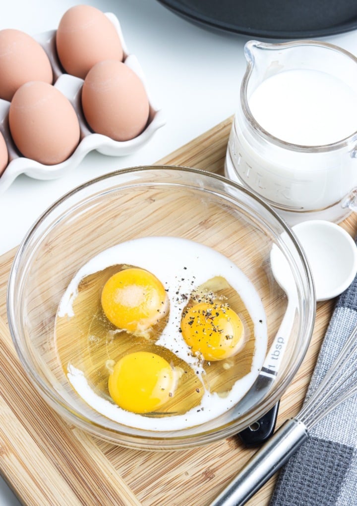 Eggs, milk, and alt and pepper in a clear mixing bowl.