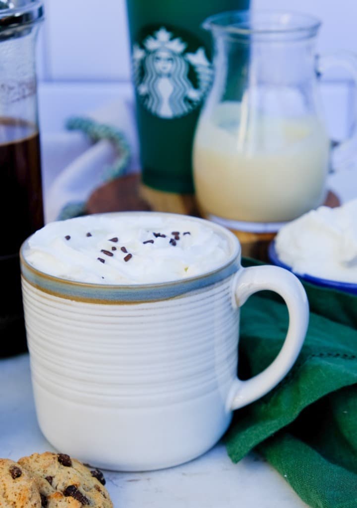 Coffee drink in a cream mug topped with whipped cream and chocolate sprinkles. 