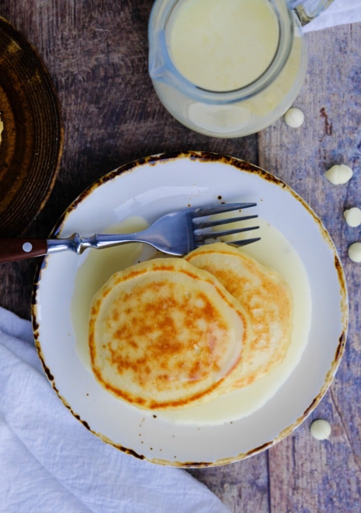 Top view on pancakes on a white plate with a fork on the side of the plate. 