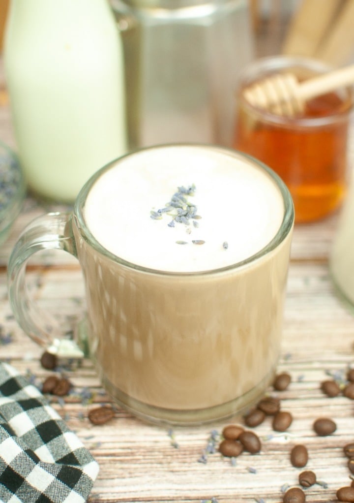 Hot lavender latte in a clear mug top with cream and small lavender buds. 