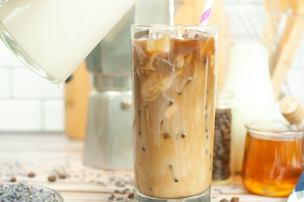 Iced lavender latte in a clear tall glass filled with ice. 