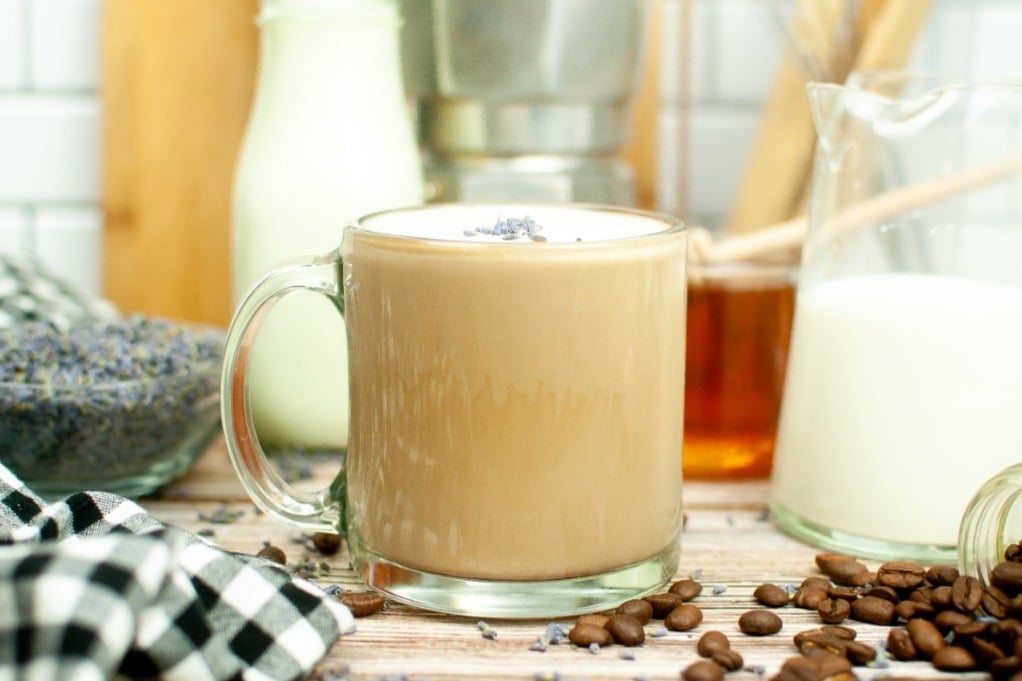 Hot coffee in a clear mug with coffee beans on the side.  