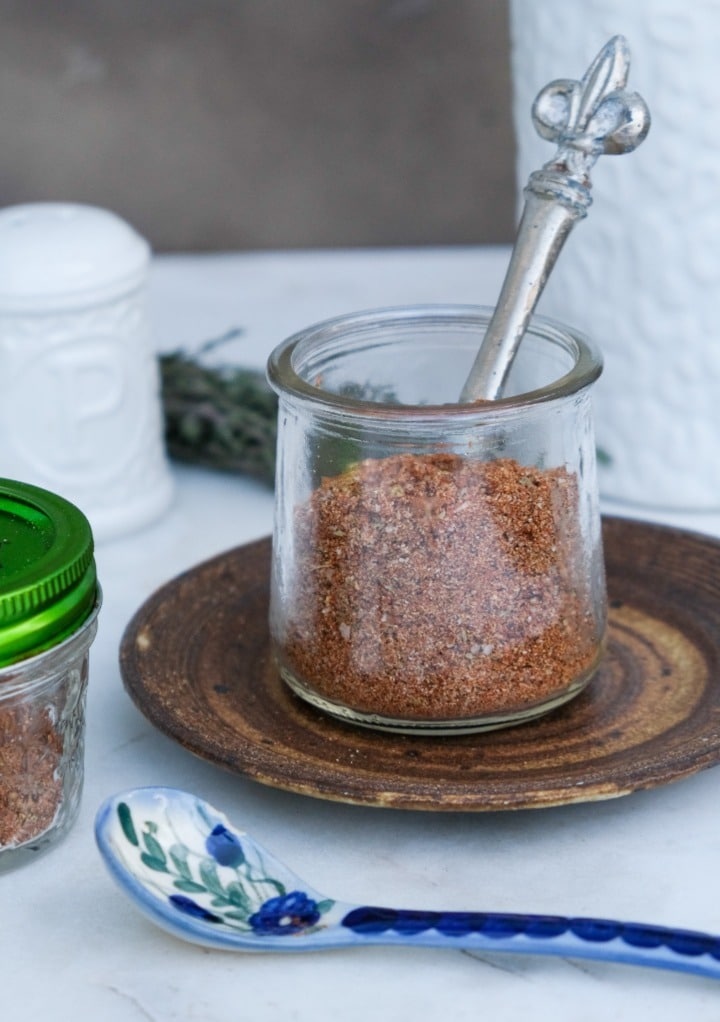 A small clear jar filled with pork rub with a spoon ready to scoop it out of the jar.