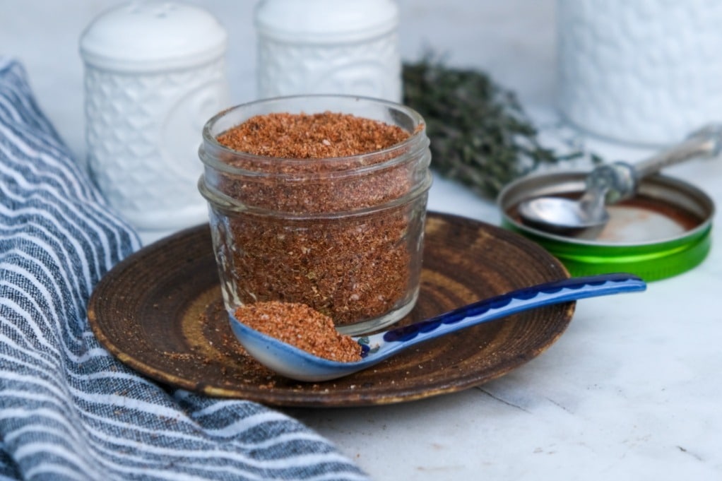 Spice rub in a mason jar with a blue spoon on the side. 