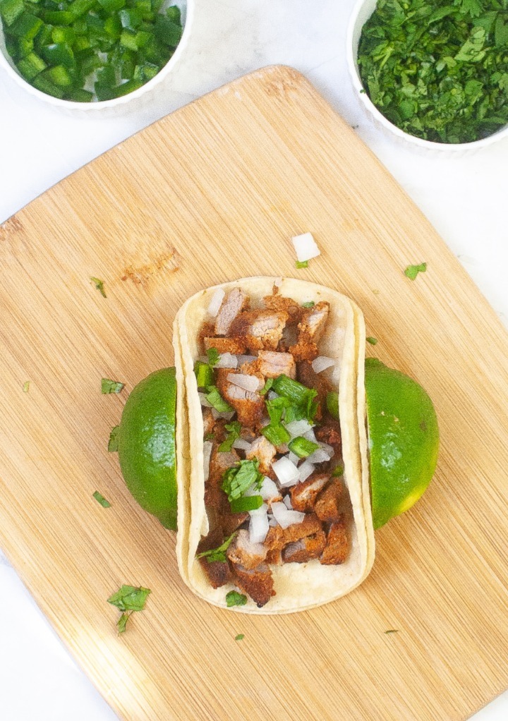 Cooked tacos on a cutting board adding toppings to the tacos. 