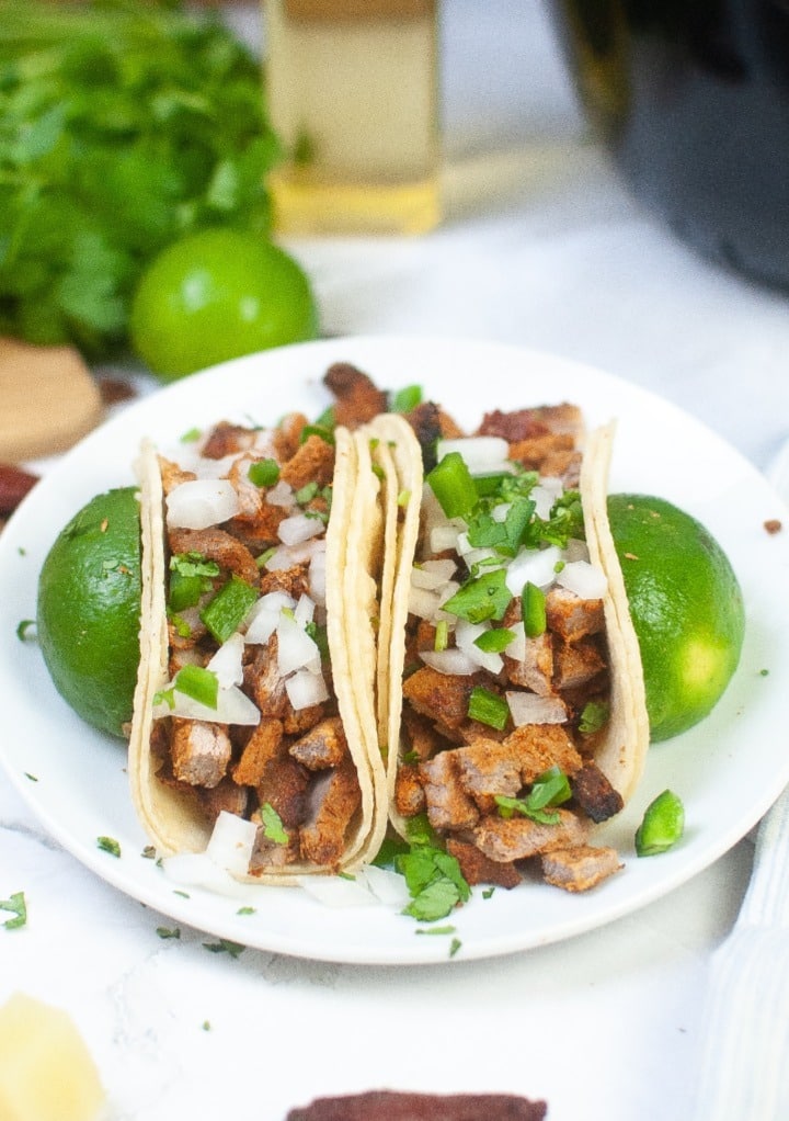 Pork tacos on a white plate topped with diced onion an jalapeno slices. 