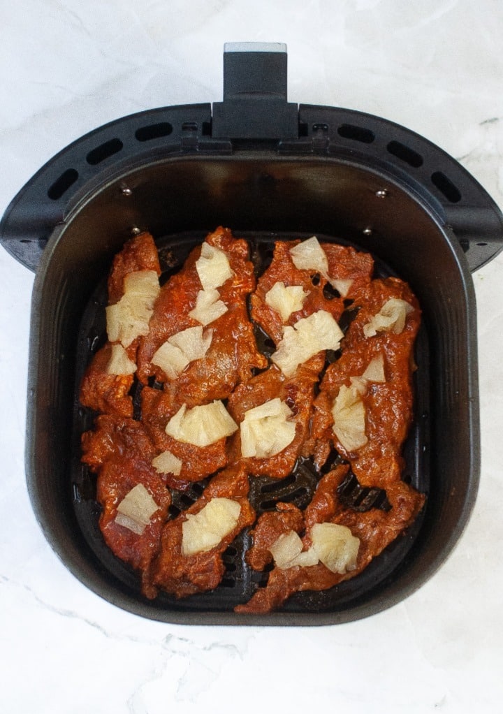 Marinated pork slices in an air fryer topped with pineapple. 