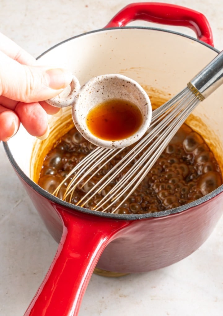 Adding vanilla extract to cooked caramel sauce.