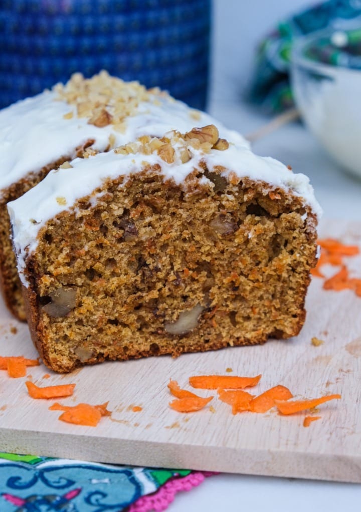 Fresh baked carrot cake loaf on a cutting board topped with cream cheese frosting. 