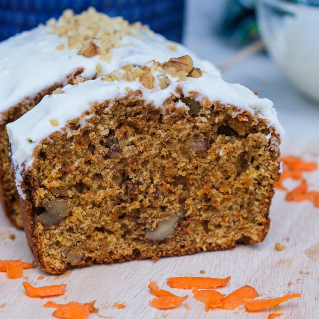 Carrot cake loaf on a cutting board topped with cream cheese frosting.