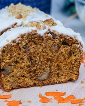 Carrot cake loaf on a cutting board topped with cream cheese frosting.