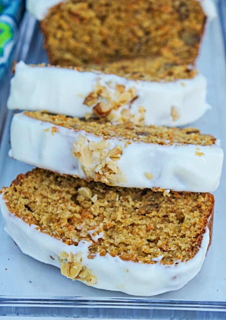 Sliced carrot cake loaf topped with frosting and chopped walnuts. 