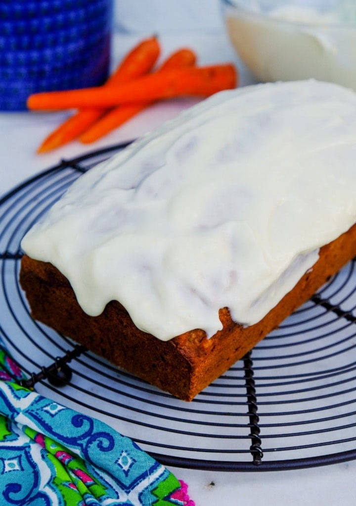 Carrot cake loaf with cream cheese frosting on a cooling rack.