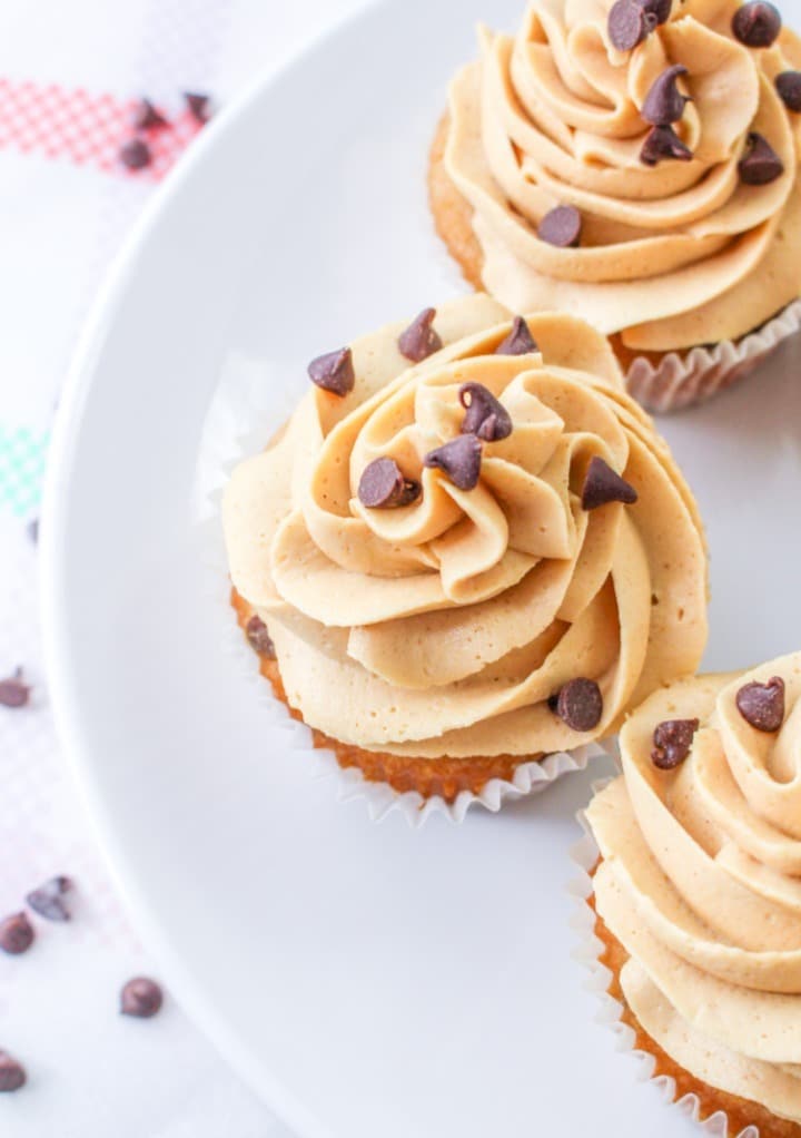 Top view of chocolate chip cupcakes with peanut butter frosting on a white serving plate. 