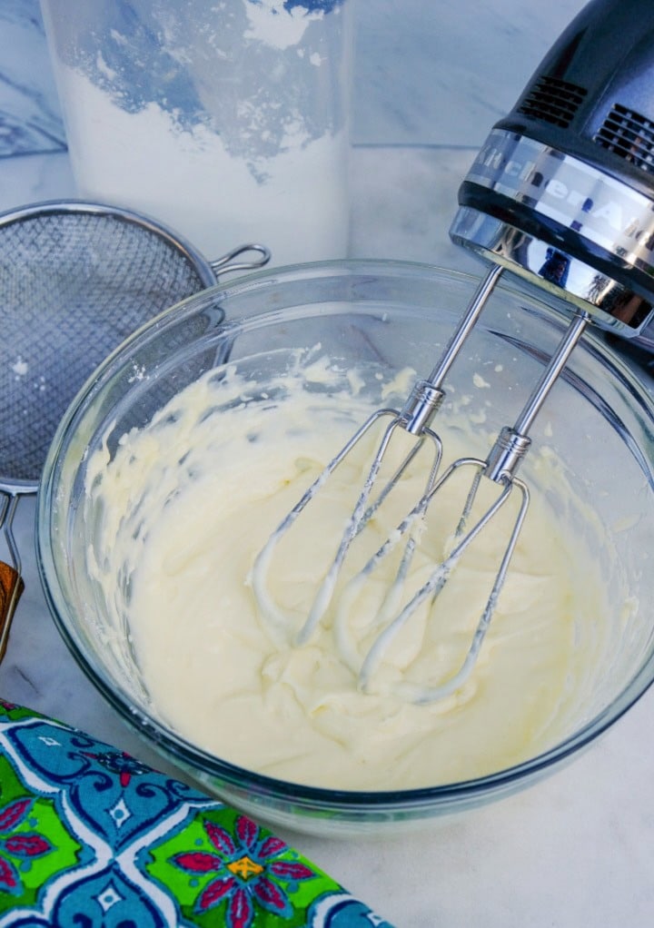 Cream cheese frosting in a mixing bowl with a hand beater combining the ingredients. 