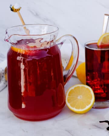 Hibiscus lemonade in a glass pitcher with glasses filled with lemonade ready to drink.